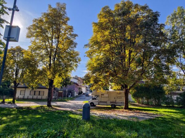 Prato e alberi dell'area sosta camper di Tarcento, vicino alle case del paese